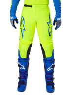 Alpinestars 2025 Fluid Haul Pants, pantaloni da motocross, giallo brillante e blu, indossati con guanti e stivali coordinati, con pannelli interni neri sulle ginocchia, loghi blu sulle cosce e design sportivo ergonomico.