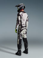 Pilota di motocross che indossa i pantaloni Alpinestars 2026 Racer Lahnd in Sand Camo e grigio, completo da gara con maglia coordinata, casco nero e stivali neri, vista posteriore che mette in evidenza il branding audace e il design ergonomico.