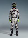 Pilota di motocross che indossa il completo Alpinestars 2026 Racer Lahnd Gear Set, tuta con motivo Sand Camo dal design bianco, grigio e nero, casco nero con occhiali verde neon, guanti verde neon brillante e stivali neri con loghi bianchi, completo coordinato per il racing off-road
