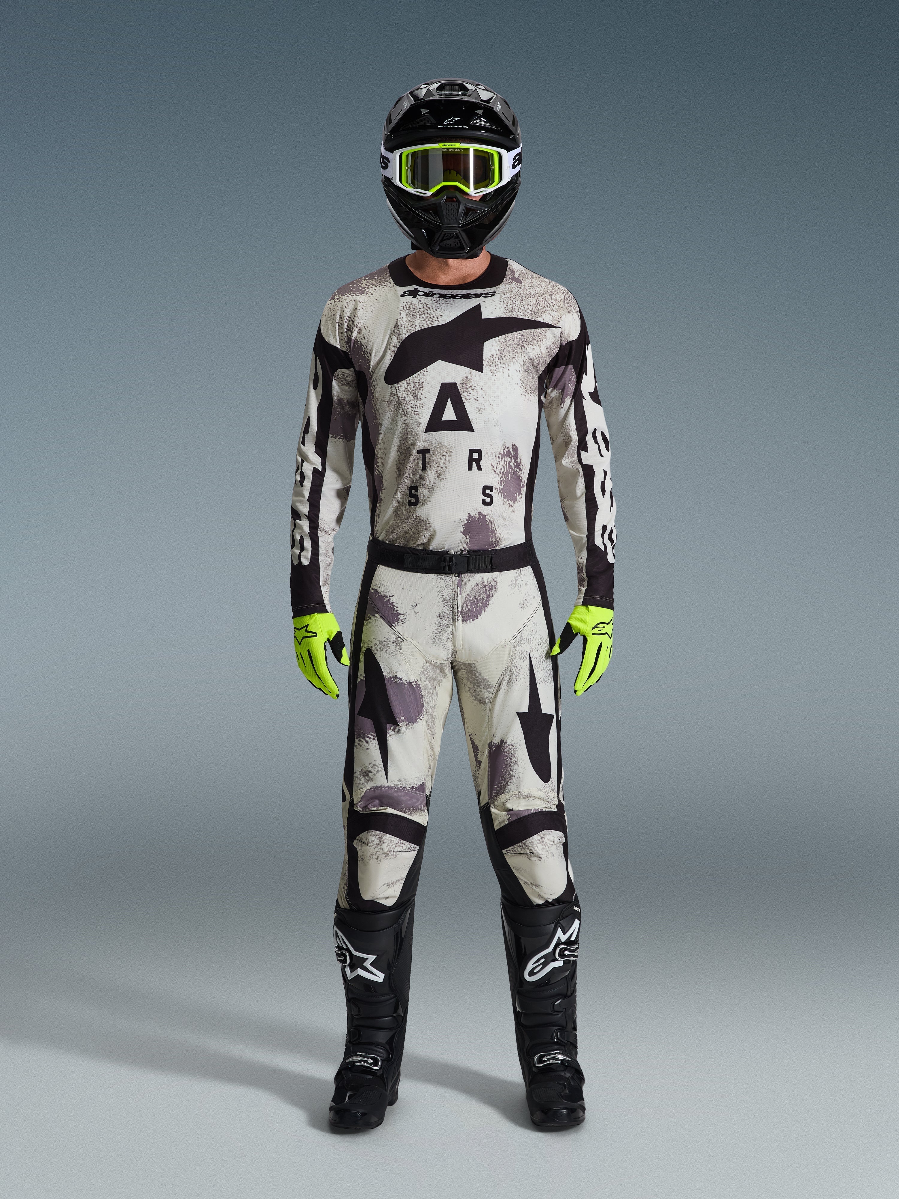 Pilota di motocross con Maglia Racer Lahnd 2026 e pantaloni coordinati in Sand Camo, casco nero con occhiali giallo neon, guanti giallo neon e stivali neri, set completo di abbigliamento da gara off-road Alpinestars