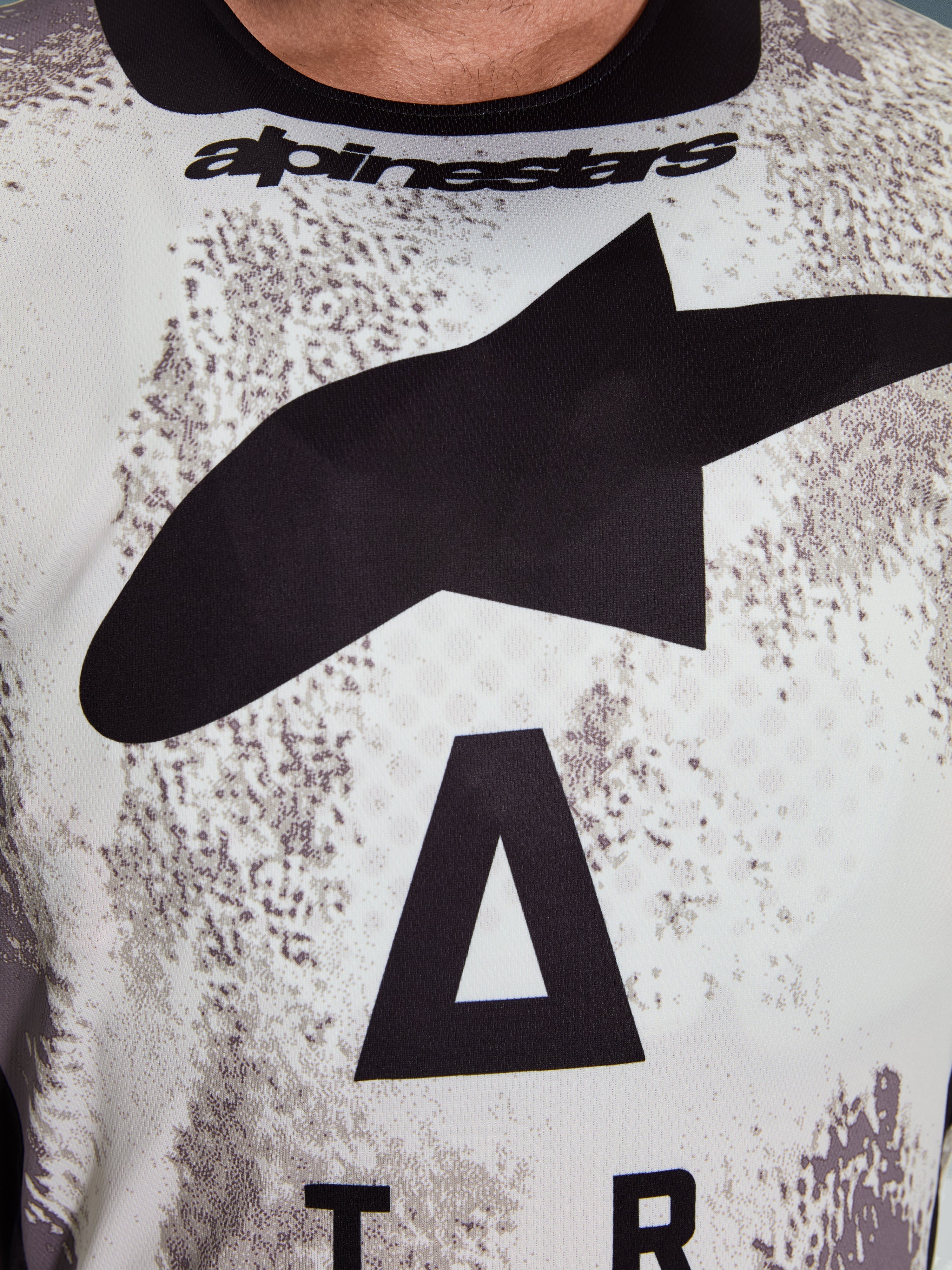 Alpinestars 2026 Racer Lahnd Jersey, primo piano dell'area del torace, motivo Sand Camo con grande logo a stella nero e scritta Alpinestars, poliestere tecnico traspirante per la guida fuoristrada
