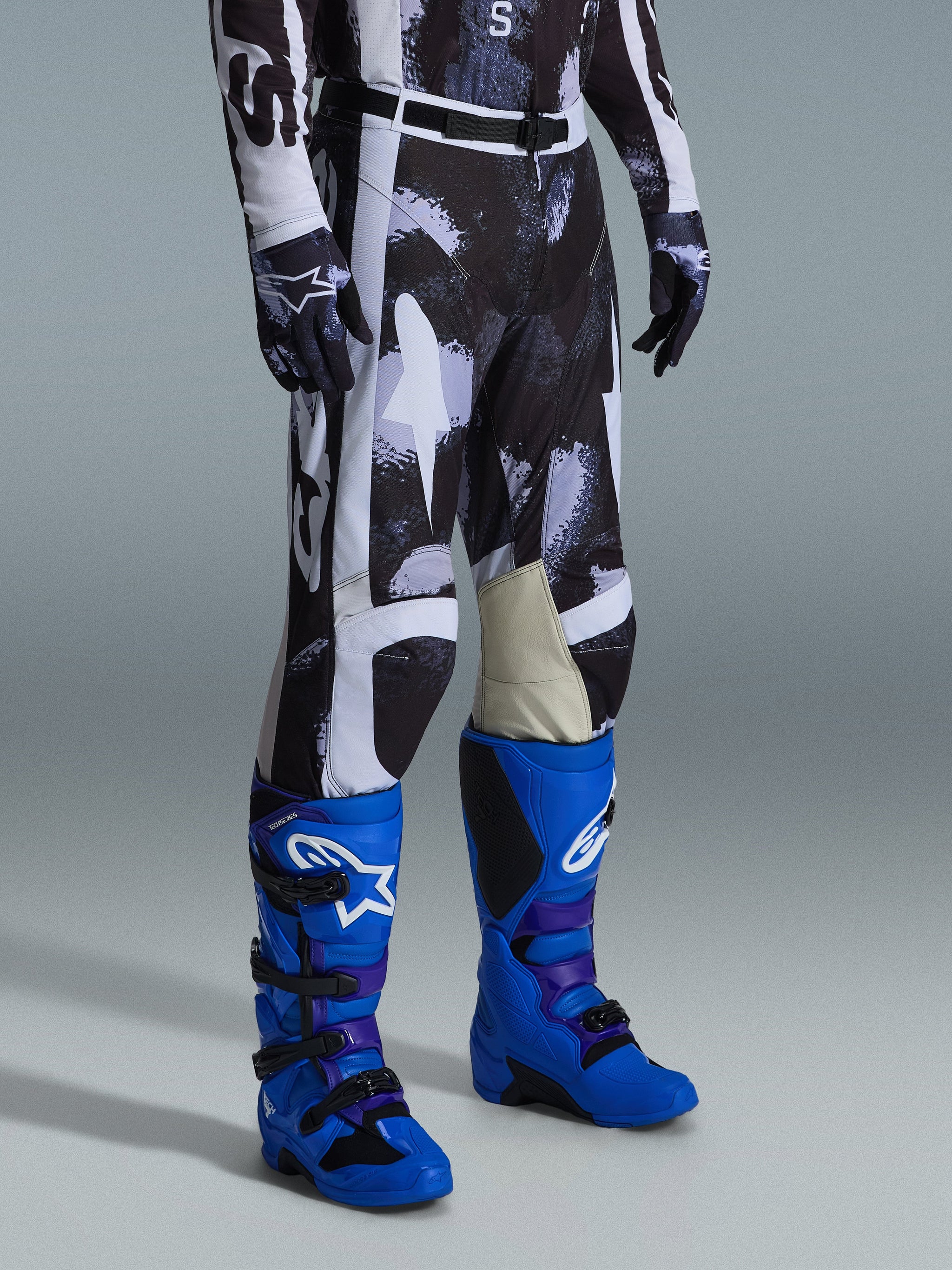 Pantaloni Alpinestars Racer Lahnd 2026, pantaloni da motocross, motivo mimetico Iron Camo grigio e nero, abbinati a stivali da gara blu acceso e guanti coordinati, con pannelli bianchi e interno ginocchia in pelle di capra, abbigliamento off-road ad alte prestazioni