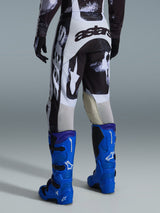 Alpinestars 2026 Racer Lahnd Pants, pantaloni da motocross, fantasia Iron Camo grigia e nera, vista posteriore con grande marchio astars bianco e nero, abbinati a stivali da motocross blu acceso, equipaggiamento professionale da corsa off-road