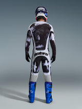 Alpinestars 2026 Racer Lahnd Pants, pantaloni da motocross, motivo Iron Camo grigio e nero, vista posteriore del pilota in tenuta da gara completa con maglia coordinata e stivali blu, progettati per prestazioni off-road