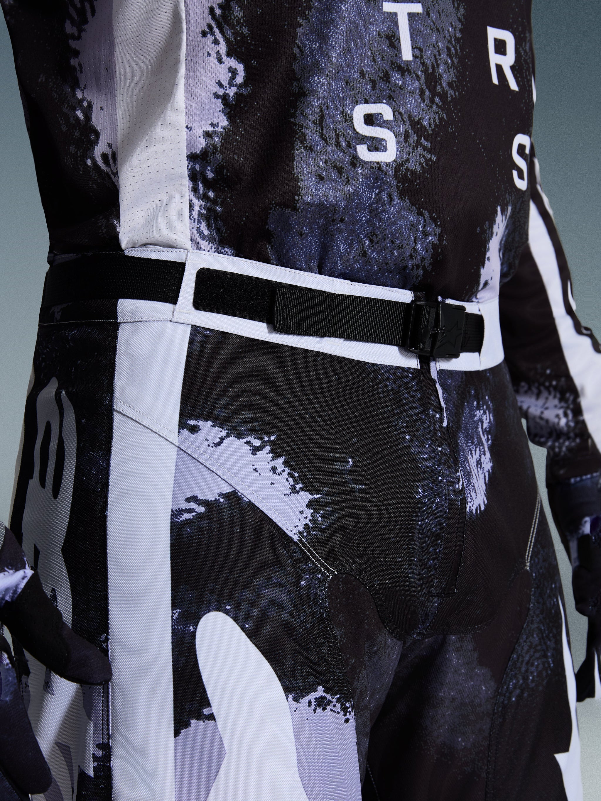 Alpinestars 2026 Racer Lahnd Pants, pantaloni da motocross in Iron Camo, vista ravvicinata della cintura regolabile in vita e della fibbia magnetica SX2, con motivo mimetico grigio e nero e resistente costruzione in polifabric 600D.