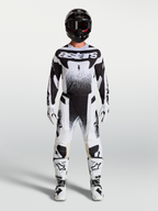 Alpinestars Pantaloni Techstar Swan e maglia, completo da motocross bianco e nero con stivali e casco coordinati su un modello, abbigliamento tecnico off-road.