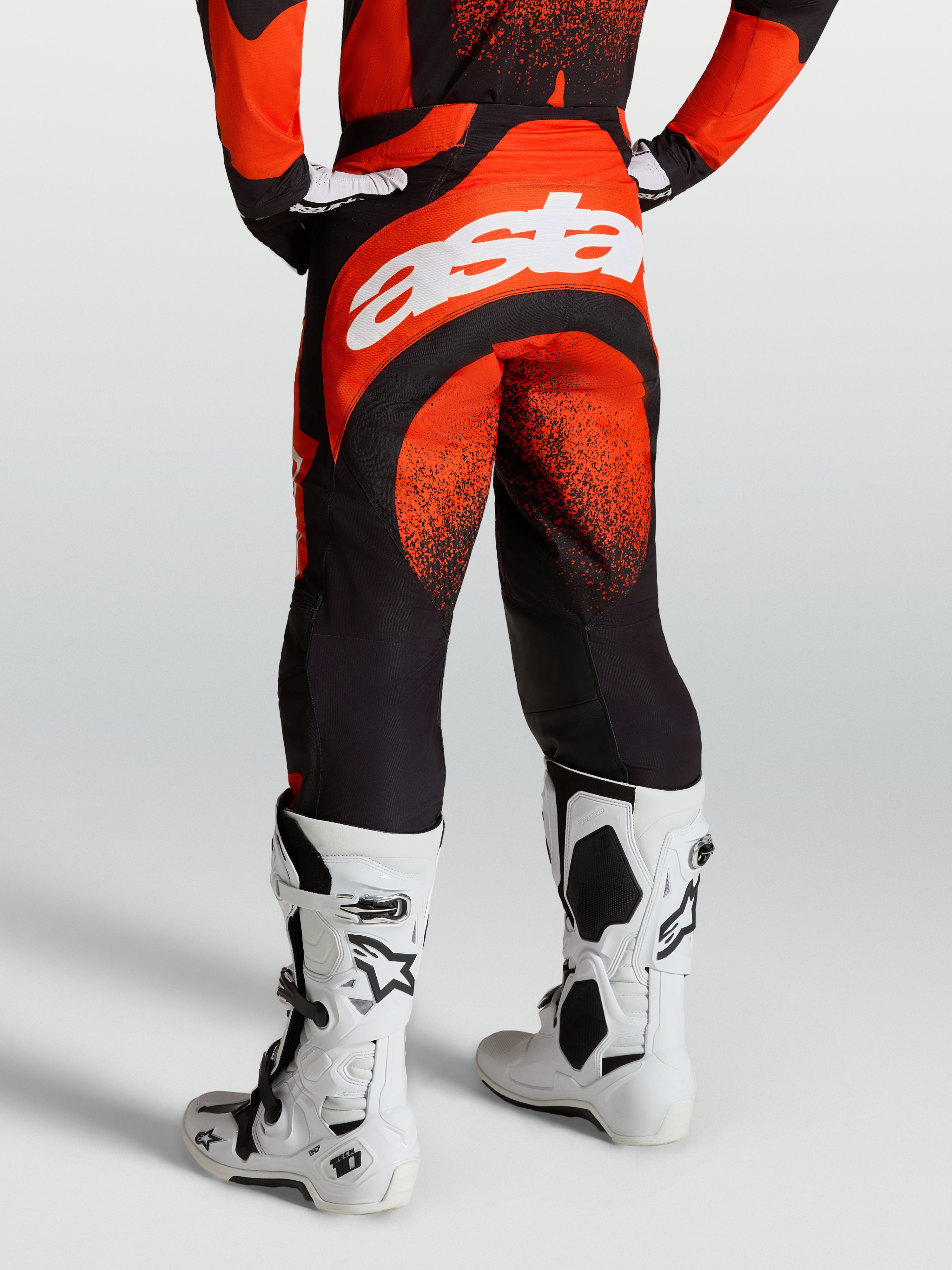 Pantaloni Techstar Swan Alpinestars, pantaloni motocross da uomo, rosso cardinale e nero, con branding Astar bianco sul retro e stivali Tech 10 bianchi.