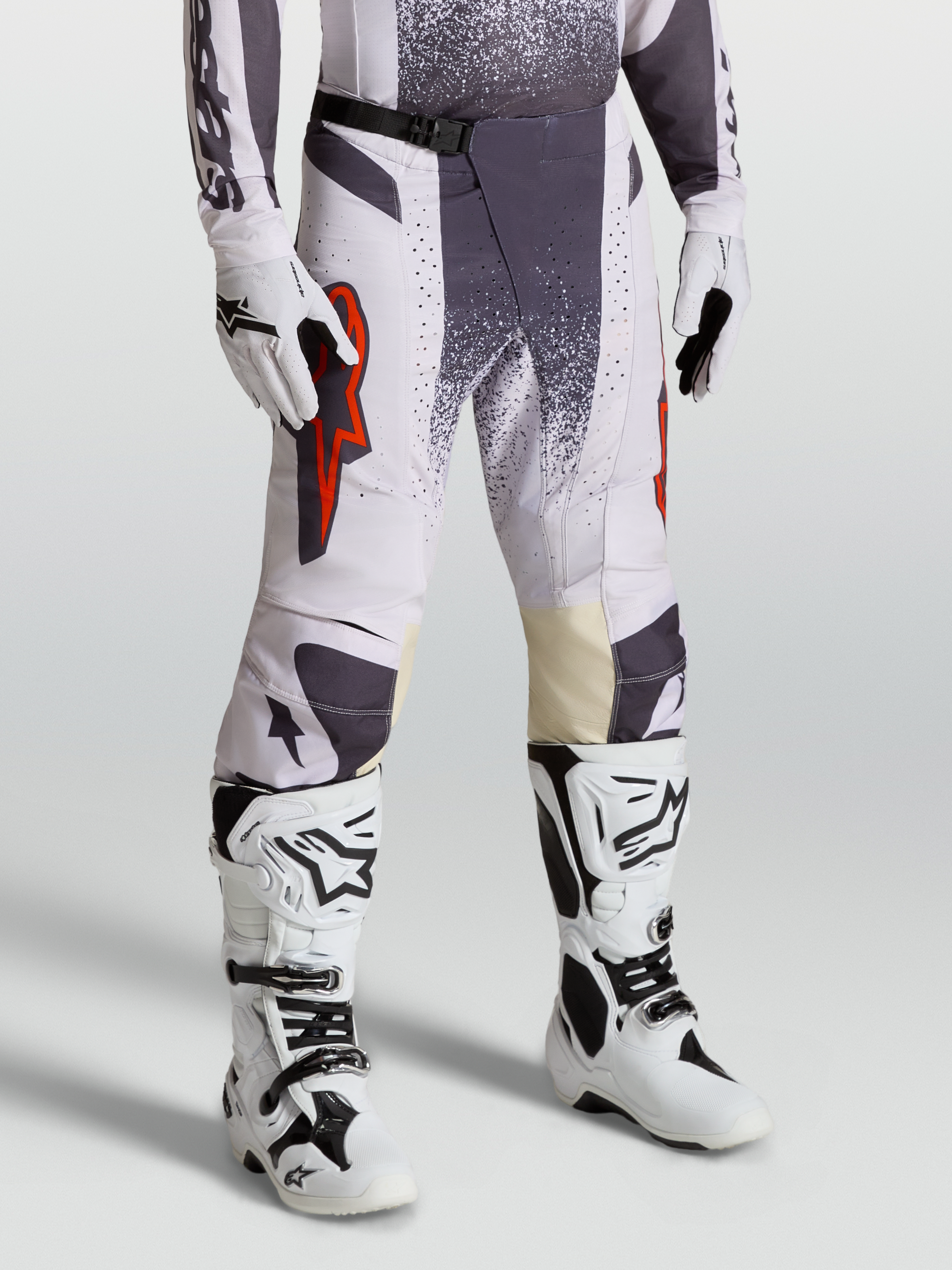 Alpinestars Pantaloni Techstar Swan, pantaloni da motocross da uomo, lilla chiaro e grigio scuro con dettagli rosso fluo, indossati con guanti e stivali bianchi, abbigliamento tecnico per off-road e competizioni