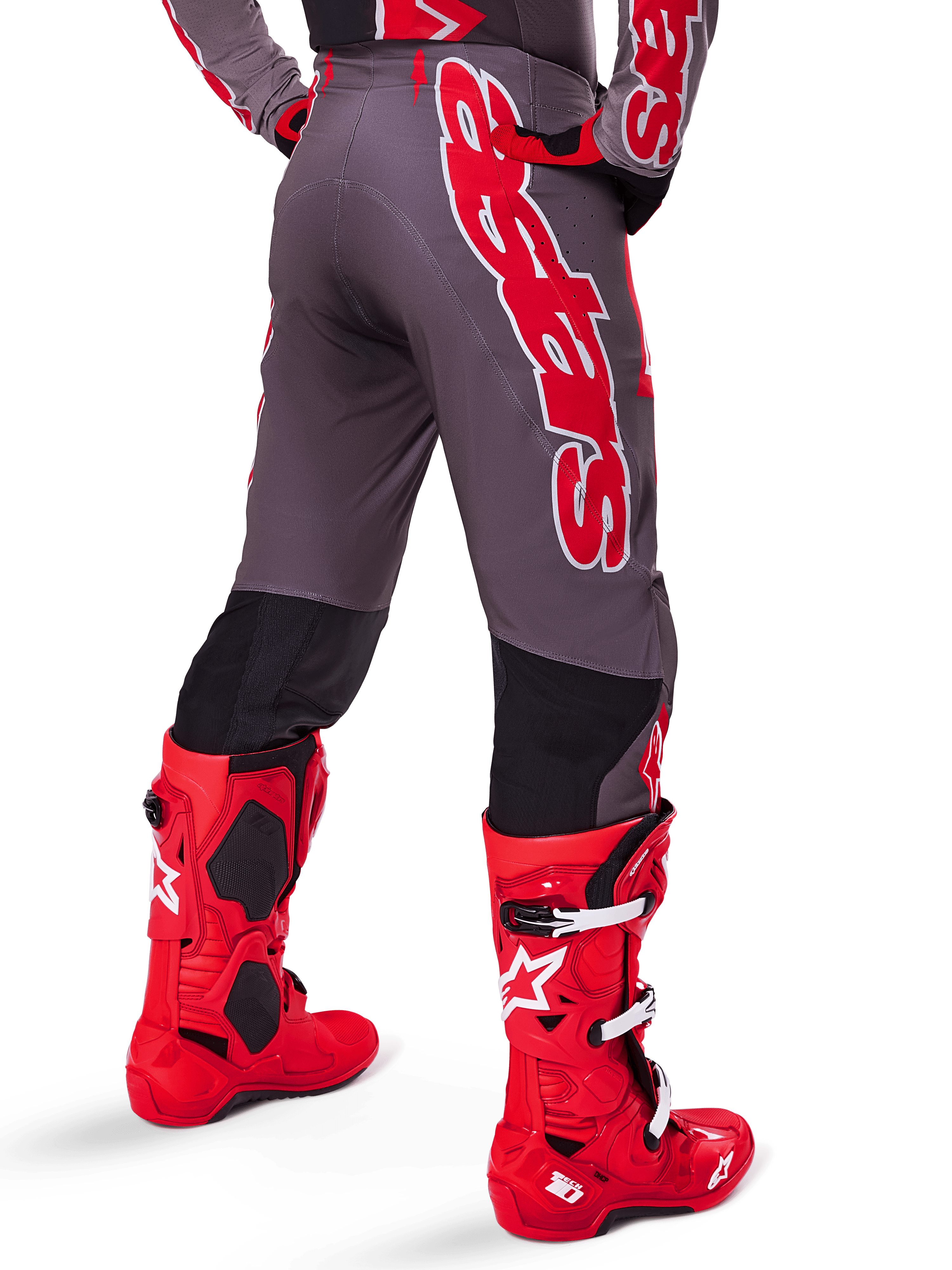Alpinestars 2025 Supertech Lipan Gear Set, vista posteriore di un pilota di motocross, pantaloni grigio scuro con grande logo verticale rosso, maglia coordinata rossa e grigia, stivali da motocross rosso acceso, abbigliamento da gara fuoristrada ad alte prestazioni