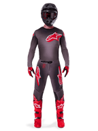 Pilota di motocross che indossa il set completo Alpinestars 2025 Supertech Lipan, Smoke Bright Red, caratterizzato da maglia e pantaloni grigio scuro con loghi rossi, casco nero con occhiali, guanti rossi e neri e stivali da motocross rosso vivace, outfit da gara professionale coordinato