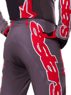 Alpinestars 2025 Supertech Lipan Pants, pantaloni da motocross, grigio e rosso acceso, primo piano di fianco e retro con grafiche del logo in rosso e bianco, perforazioni per la ventilazione e vestibilità atletica da gara indossati con abbigliamento coordinato.