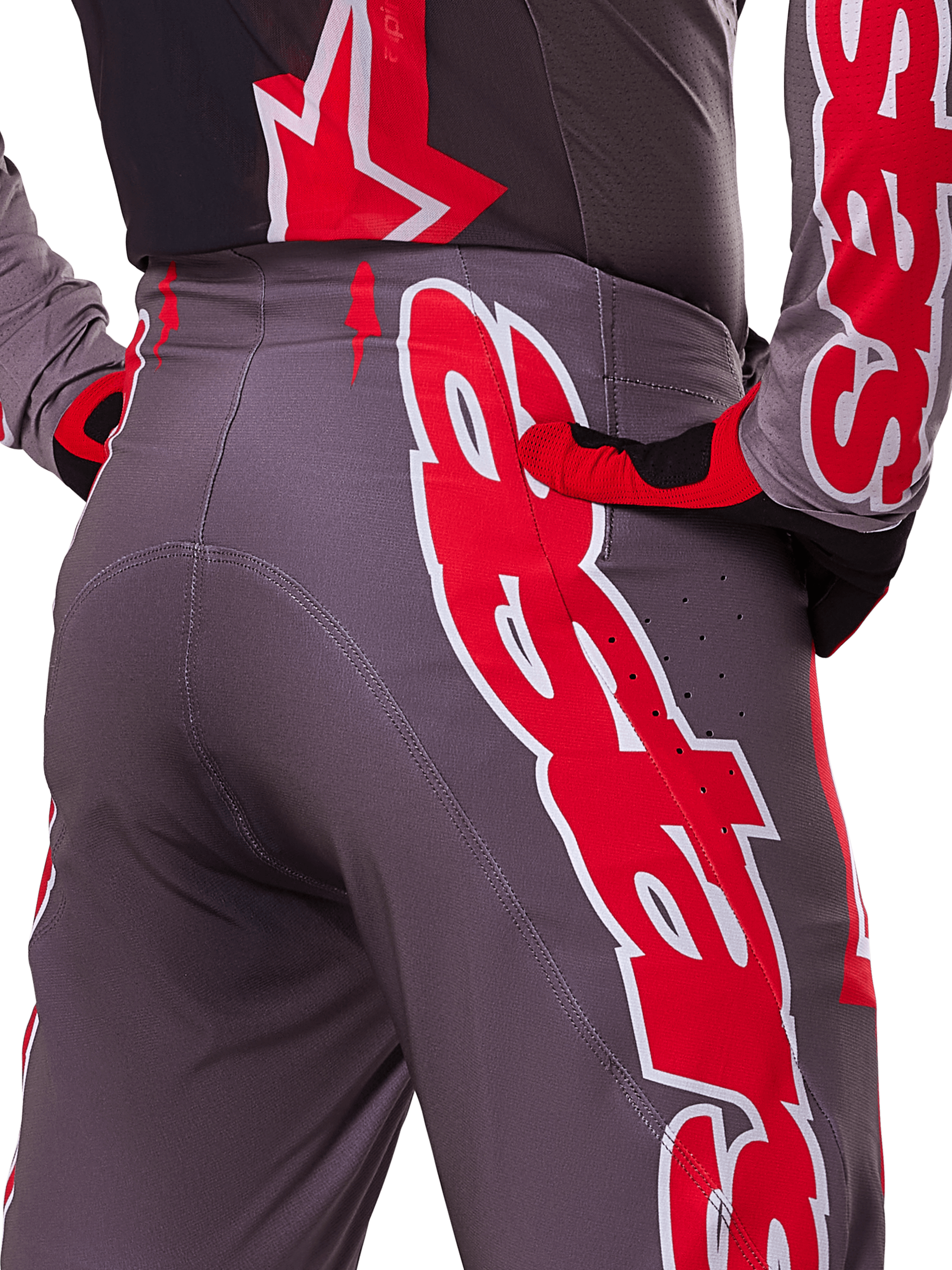 Alpinestars 2025 Supertech Lipan Pants, pantaloni da motocross, grigio e rosso acceso, primo piano di fianco e retro con grafiche del logo in rosso e bianco, perforazioni per la ventilazione e vestibilità atletica da gara indossati con abbigliamento coordinato.