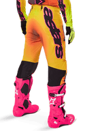 Alpinestars 2025 Supertech Lipan Gear Set, vista posteriore di pantaloni da motocross con sfumatura giallo e arancione e branding nero audace, abbinati a stivali Tech 10 rosa acceso e guanti gialli, attrezzatura professionale per corse fuoristrada
