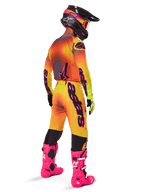 Pilota di motocross visto da dietro, pantaloni Alpinestars 2025 Supertech Lipan con sfumatura giallo e rosa, maglia coordinata, stivali rosa acceso e casco nero con accenti rosa, completo professionale per gare off-road