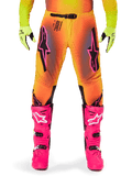 Pantaloni Alpinestars Supertech Lipan 2025, pantaloni da motocross, sfumatura arancione e gialla con accenti rosa e neri, indossati con stivali rosa acceso e guanti giallo neon, dotati di ventilazione tagliata al laser e fibbia sicura in vita, completo da gara professionale
