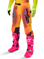 Alpinestars 2025 Supertech Lipan Gear Set, pantaloni da motocross, sfumatura giallo e arancione con accenti rosa e viola, con vistosi loghi Alpinestars neri sulle cosce, indossati con guanti gialli e stivali da motocross rosa acceso.