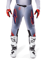 Pantaloni Alpinestars Supertech Lipan 2025, pantaloni da motocross, grigio e arancione fluo, indossati con guanti rossi e neri e stivali bianchi e neri, con grandi loghi a stella Alpinestars sulle cosce e perforazioni per la ventilazione per gare di livello professionale.