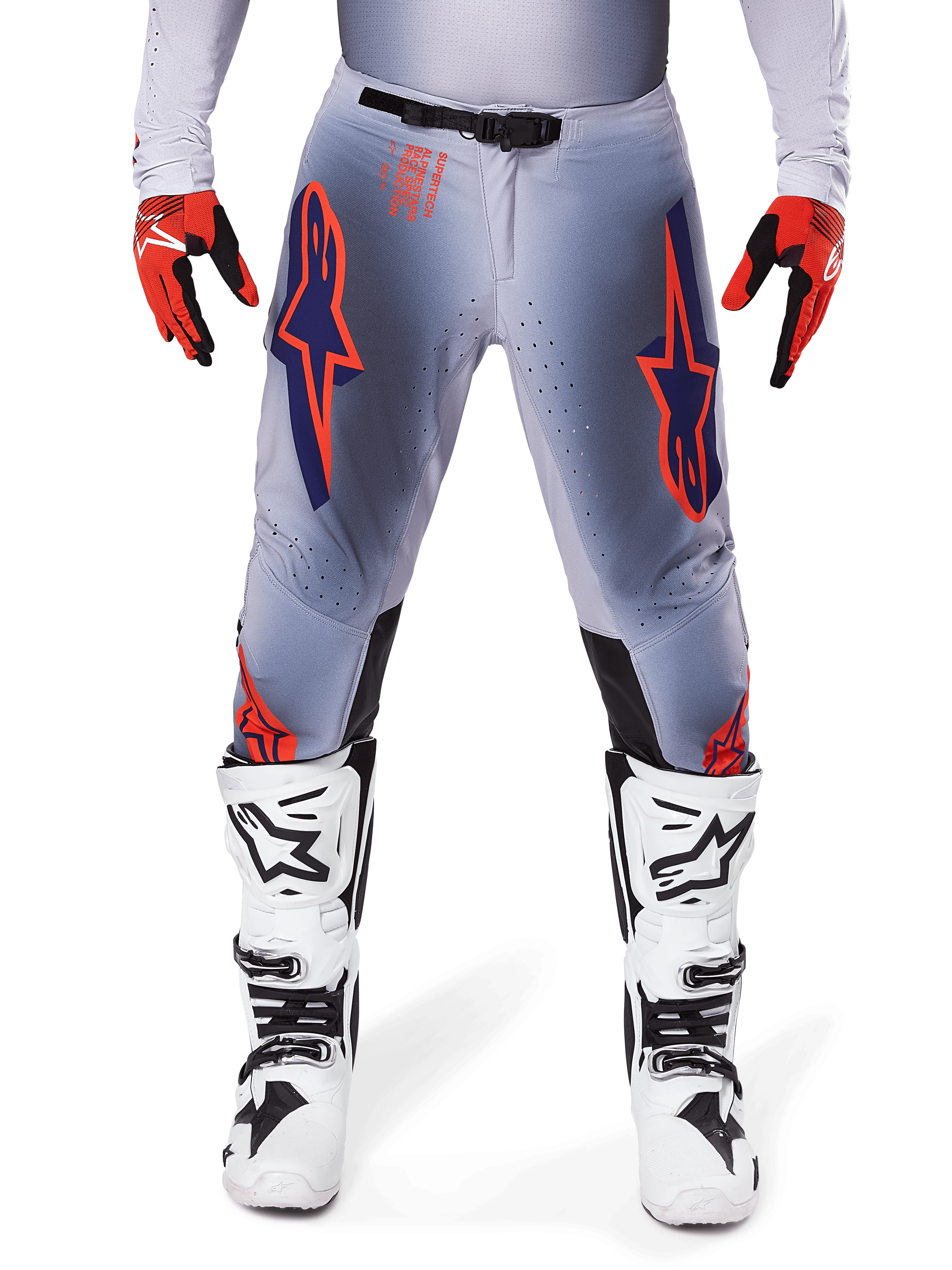 Pantaloni Alpinestars Supertech Lipan 2025, pantaloni da motocross, grigio e arancione fluo, indossati con guanti rossi e neri e stivali bianchi e neri, con grandi loghi a stella Alpinestars sulle cosce e perforazioni per la ventilazione per gare di livello professionale.