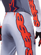 Alpinestars 2025 Supertech Lipan Pants and Jersey, set abbigliamento motocross, grigio e arancione fluo, primo piano del lato e del retro con grande marchio Alpinestars arancione, tessuto rip-stop ad alte prestazioni con ventilazione traforata