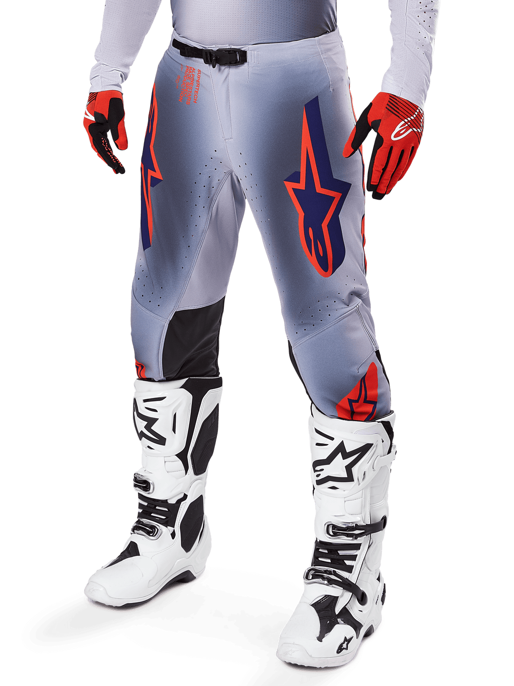 Pantaloni Alpinestars Supertech Lipan 2025, pantaloni da motocross, grigio e arancione fluo, con design a stelle blu navy e pannelli interni neri sulle ginocchia, indossati con guanti rosso-arancio e stivali bianchi, abbigliamento professionale da gara fuoristrada