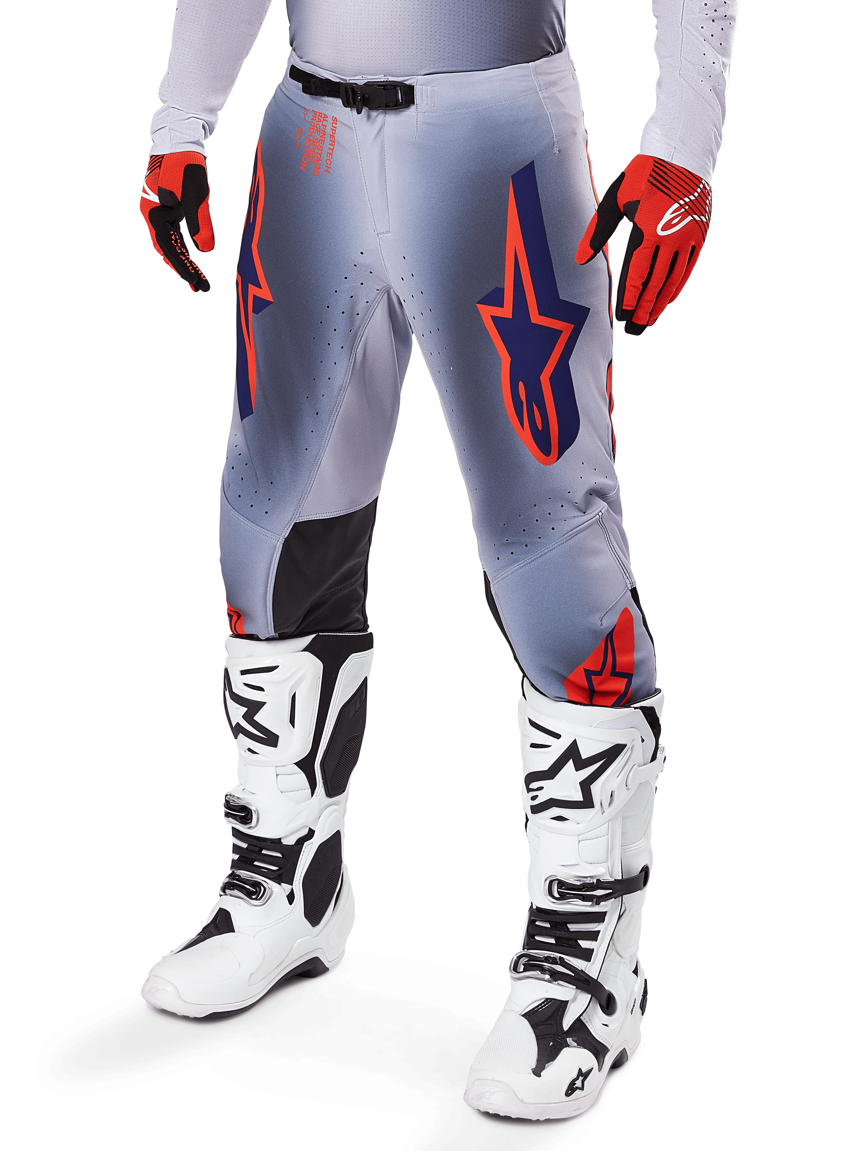 Pantaloni Alpinestars Supertech Lipan 2025, pantaloni da motocross, grigio e arancione fluo, con design a stelle blu navy e pannelli interni neri sulle ginocchia, indossati con guanti rosso-arancio e stivali bianchi, abbigliamento professionale da gara fuoristrada