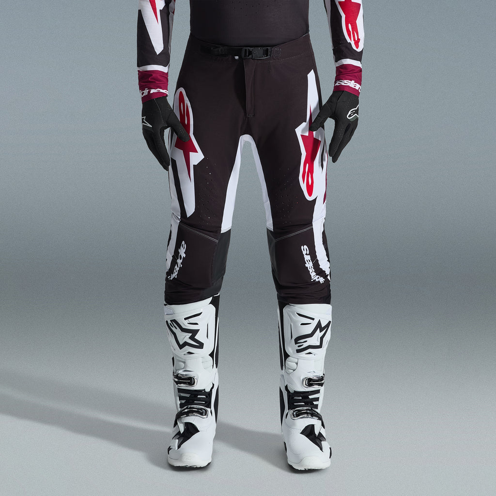 Alpinestars 2026 Supertech AFD Vista Gear Set, pilota di motocross con pantaloni neri e grandi loghi bianchi e rossi, maglia tecnica coordinata con polsini bordeaux, guanti neri e stivali da gara professionali bianchi, completo da gara fuoristrada ad alte prestazioni