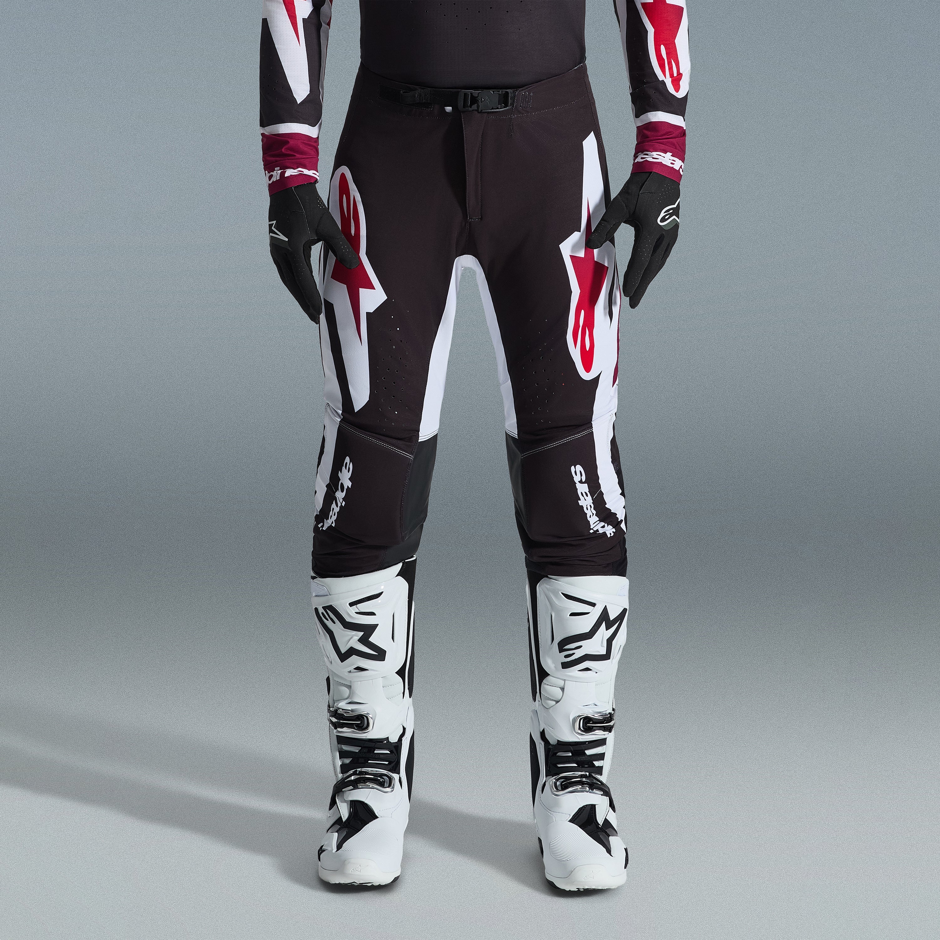 Alpinestars 2026 Supertech AFD Vista Gear Set, pilota di motocross con pantaloni neri e grandi loghi bianchi e rossi, maglia tecnica coordinata con polsini bordeaux, guanti neri e stivali da gara professionali bianchi, completo da gara fuoristrada ad alte prestazioni
