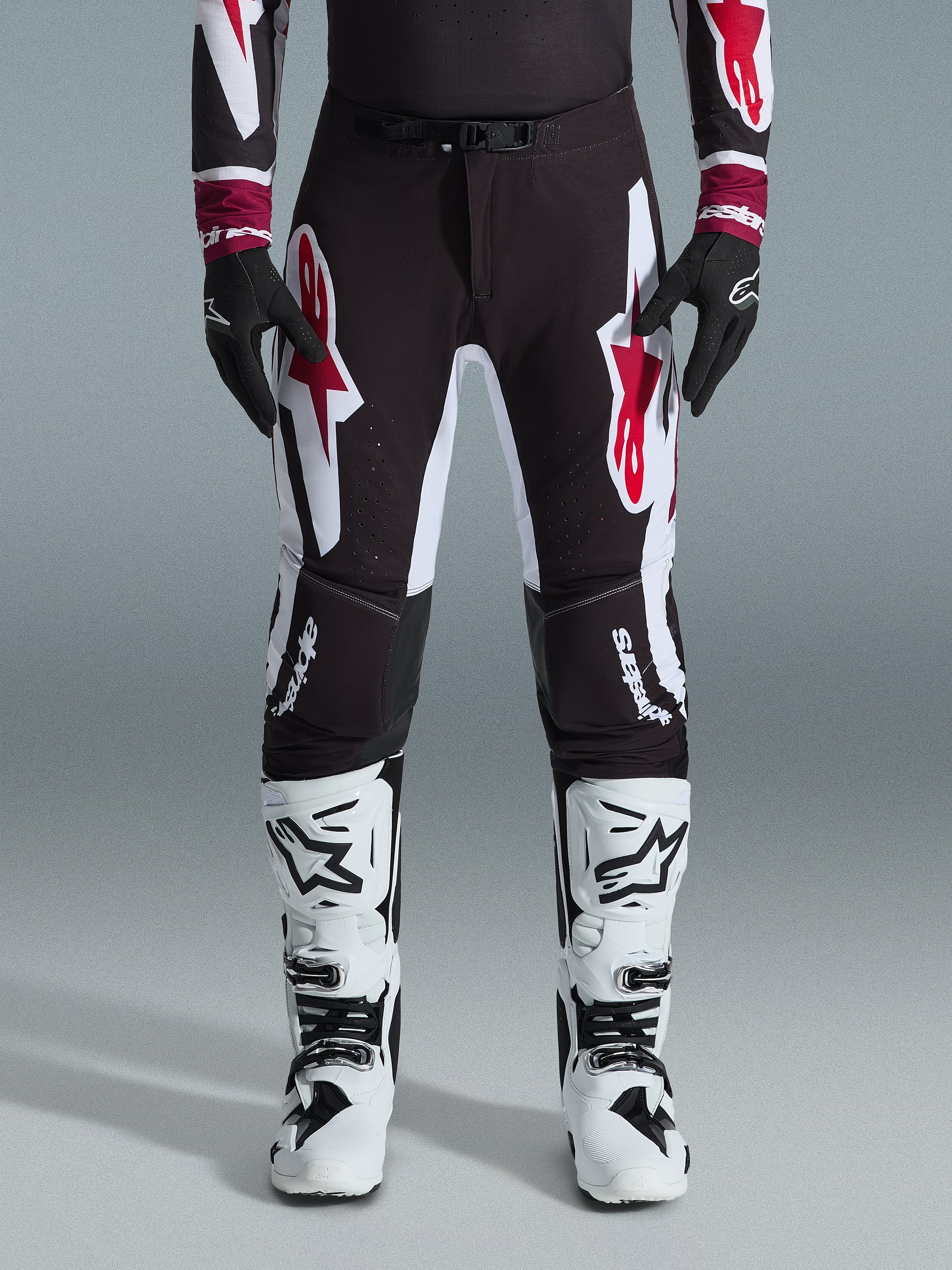 Alpinestars 2026 Supertech AFD Vista Pants, pantaloni da motocross, nero rosso e bianco, con grandi loghi grafici sulle cosce e sulle ginocchia, indossati con stivali da gara bianchi e guanti neri, design atletico race-ready per competizioni off-road d'élite