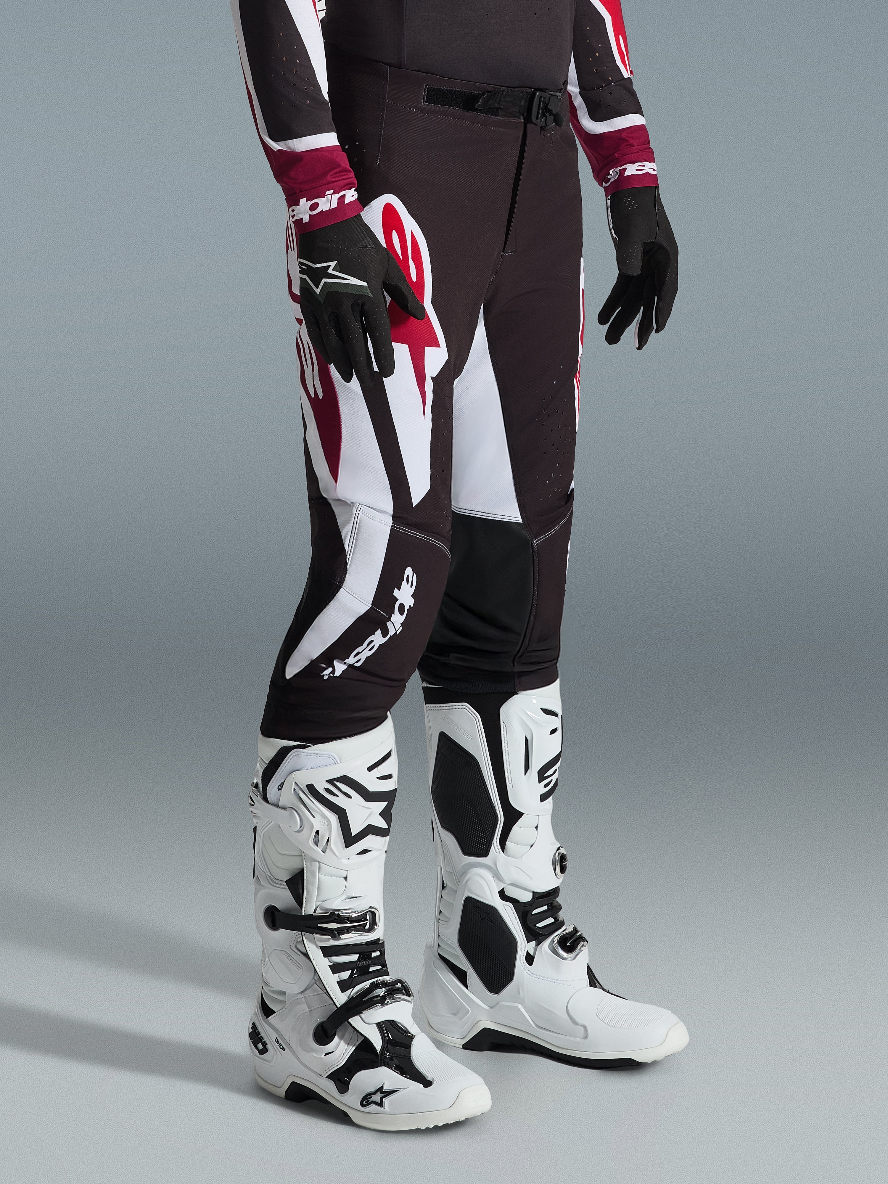 Alpinestars Supertech AFD Vista Pants 2026, pantaloni da motocross, nero, rosso e bianco, con grafiche audaci e loghi, indossati con stivali off-road bianchi e neri e guanti neri, vestibilità atletica professionale.