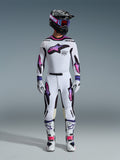 Pilota di motocross che indossa il completo Alpinestars 2026 Supertech AFD Vista, maglia e pantaloni bianchi con grafiche a stella sfumate rosa e viola, casco nero con occhiali coordinati, stivali bianchi con accenti rosa e guanti bianchi, abbigliamento professionale coordinato per gare fuoristrada