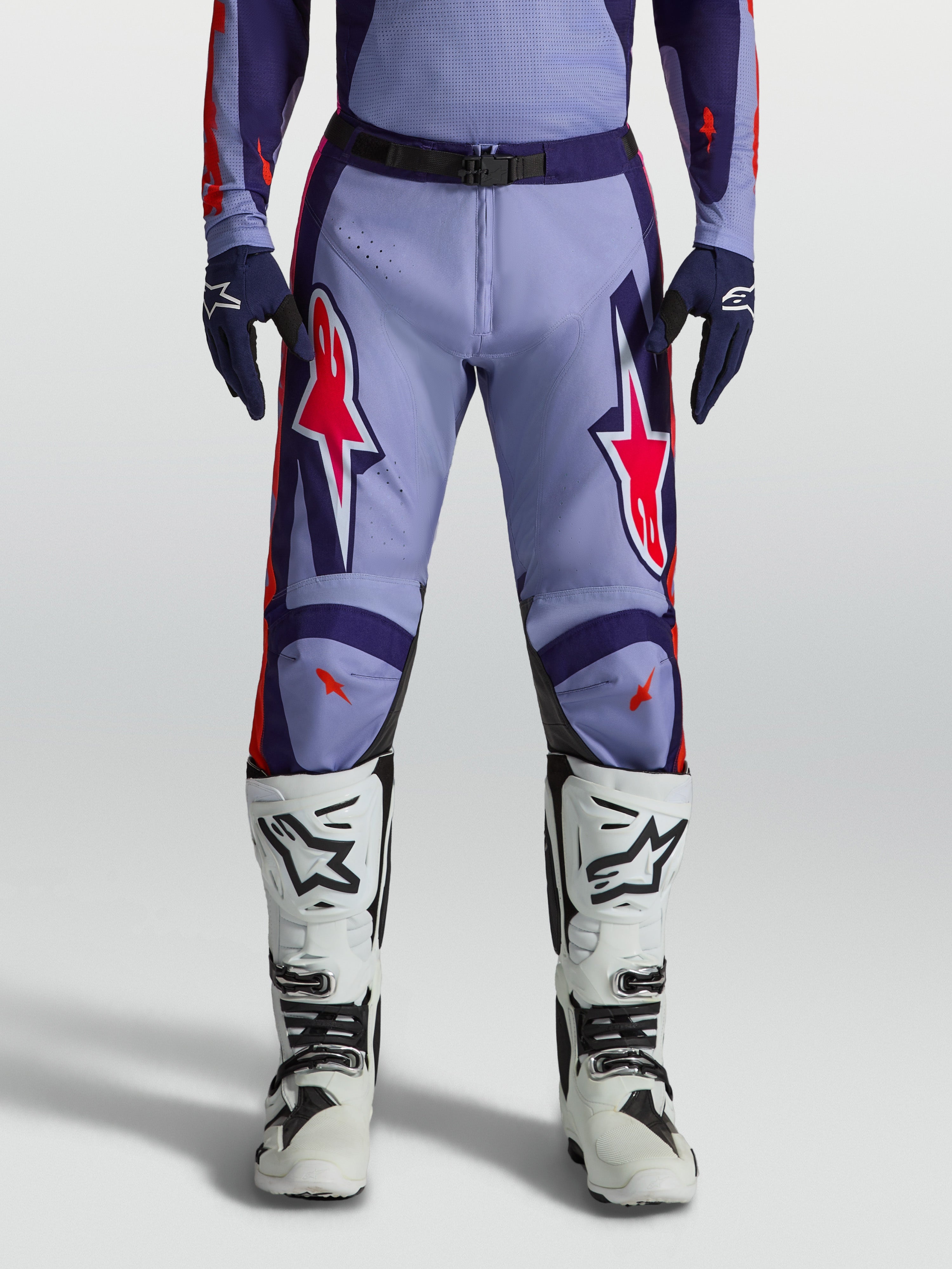 Alpinestars pantaloni Racer Air Hunt, pantaloni da motocross uomo viola e rosa fluo, indossati con stivali bianchi.