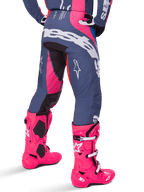 Alpinestars Techstar Dreem Pants 2025, pantaloni da motocross, grigio e rosa multicolore, vista posteriore con grande marchio Alpinestars bianco sulla seduta, indossati con stivali Tech 10 rosa brillante coordinati, equipaggiamento da gara off-road durevole con pannelli rinforzati.