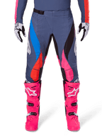 Alpinestars Pantaloni Techstar Dreem 2025, pantaloni da motocross, grigio multicolor con accenti rosa, blu e arancione, indossati con stivali da motocross rosa acceso e maglia coordinata, vestibilità atletica da gara con fori di ventilazione tagliati al laser