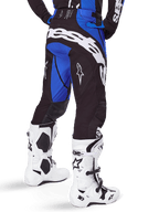 Alpinestars 2025 Techstar Dreem Pants, pantaloni da motocross, nero e blu, vista posteriore con audace marchio Alpinestars bianco sulla seduta, indossati con stivali da motocross bianchi e neri e maglia blu coordinata, vestibilità atletica per gare fuoristrada