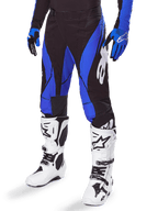 Alpinestars 2025 Techstar Dreem Pants, pantaloni da motocross, nero e blu, indossati con stivali da motocross bianchi e guanti blu, con logo Alpinestars bianco sulla gamba, costruzione resistente per gare fuoristrada