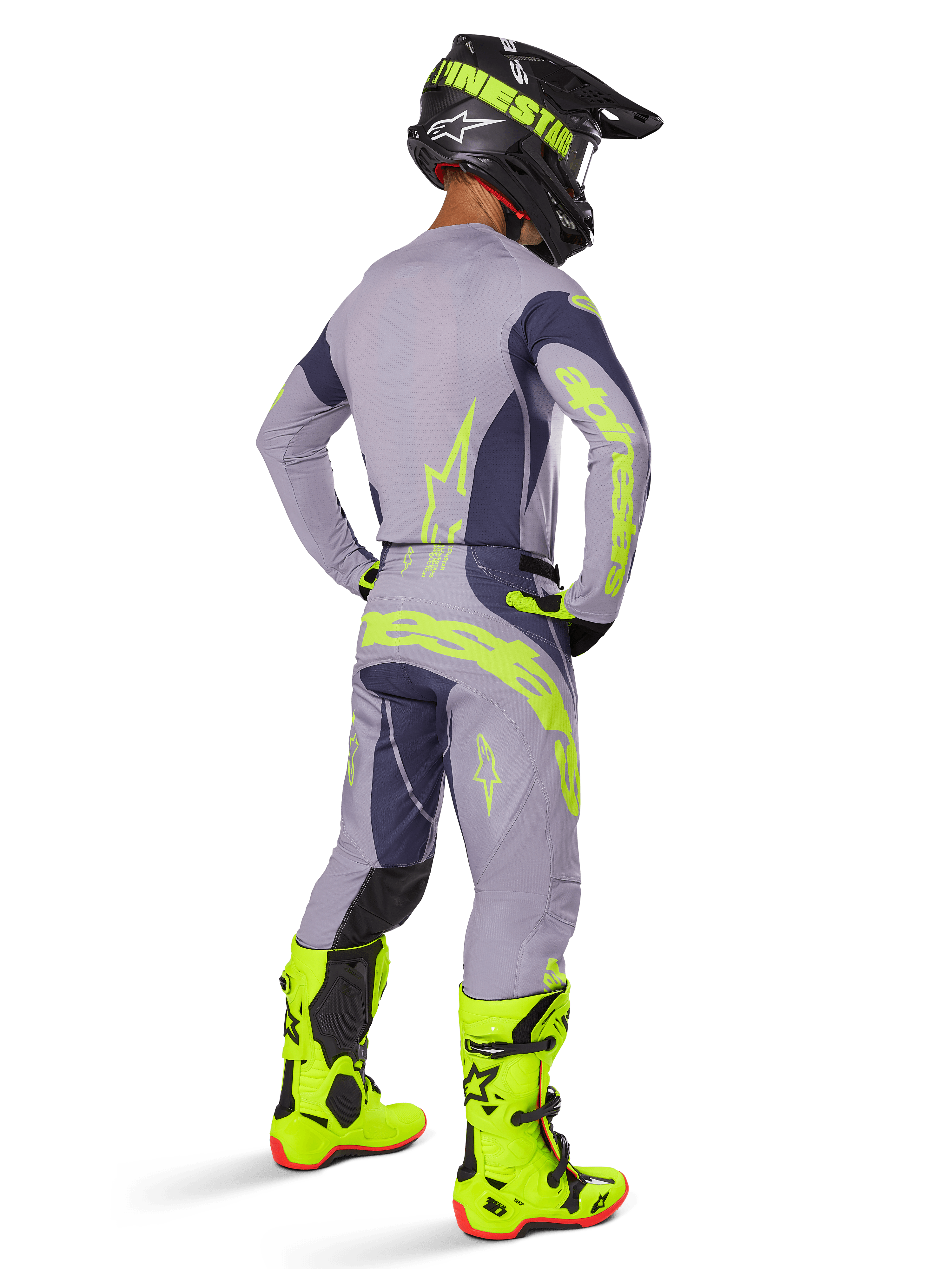 Pilota di motocross visto da dietro con equipaggiamento da gara completo, inclusi pantaloni Alpinestars 2025 Techstar Dreem in grigio e grigio scuro con vivaci accenti giallo neon, maglia grigia coordinata con grafiche neon, stivali giallo neon brillante e casco nero, outfit professionale da motocross coordinato