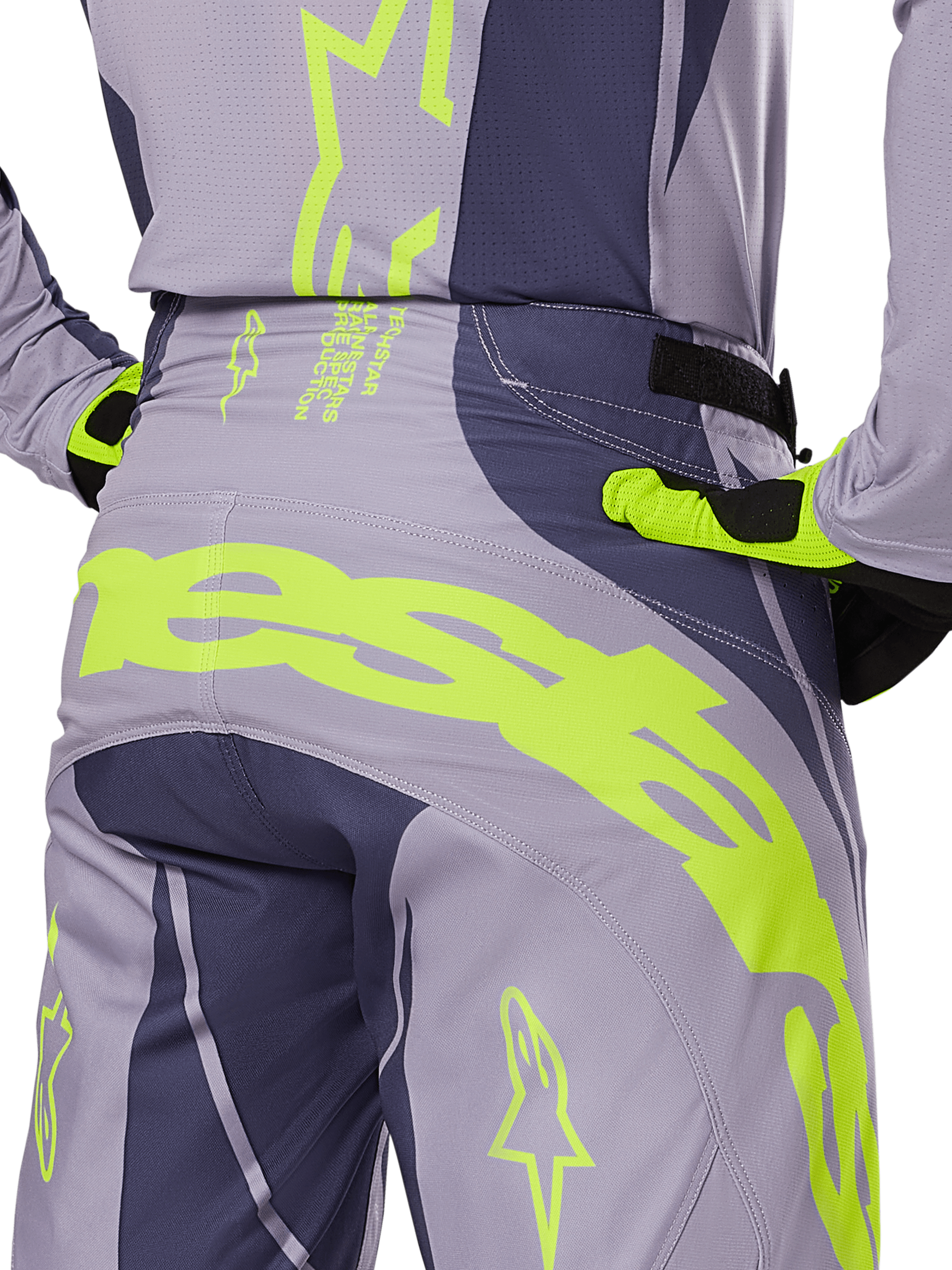Alpinestars 2025 Techstar Dreem Pants, pantaloni da motocross, grigio e grigio scuro con accenti giallo fluorescente, vista posteriore con marchio Alpinestars sul carré, indossati con maglia e guanti coordinati, progettati per gare fuoristrada