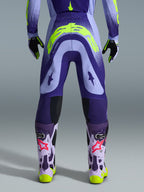 Alpinestars 2026 Supertech Scenz Pants, pantaloni da motocross, viola e giallo fluo, vista posteriore con grande logo giallo sulla seduta, indossati con maglia, guanti e stivali protettivi coordinati, vestibilità atletica per gare di motocross professionistiche