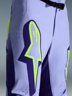 Alpinestars Pantaloni Supertech Scenz 2026, pantaloni da motocross, viola e giallo fluo, primo piano con grande logo giallo sulla coscia, perforazioni tagliate al laser per la ventilazione e fibbia magnetica in vita, abbigliamento off-road con vestibilità atletica
