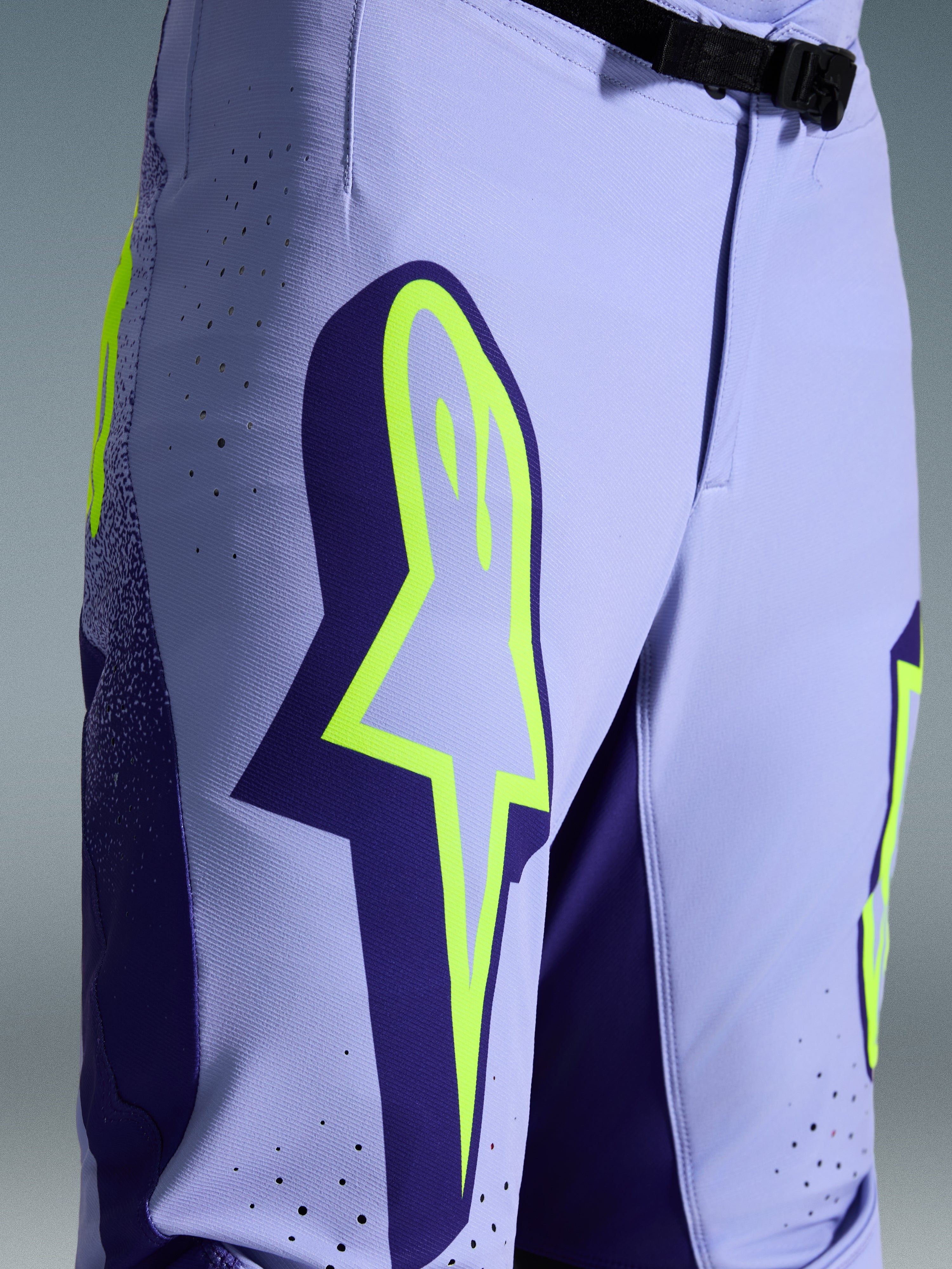 Alpinestars Pantaloni Supertech Scenz 2026, pantaloni da motocross, viola e giallo fluo, primo piano con grande logo giallo sulla coscia, perforazioni tagliate al laser per la ventilazione e fibbia magnetica in vita, abbigliamento off-road con vestibilità atletica