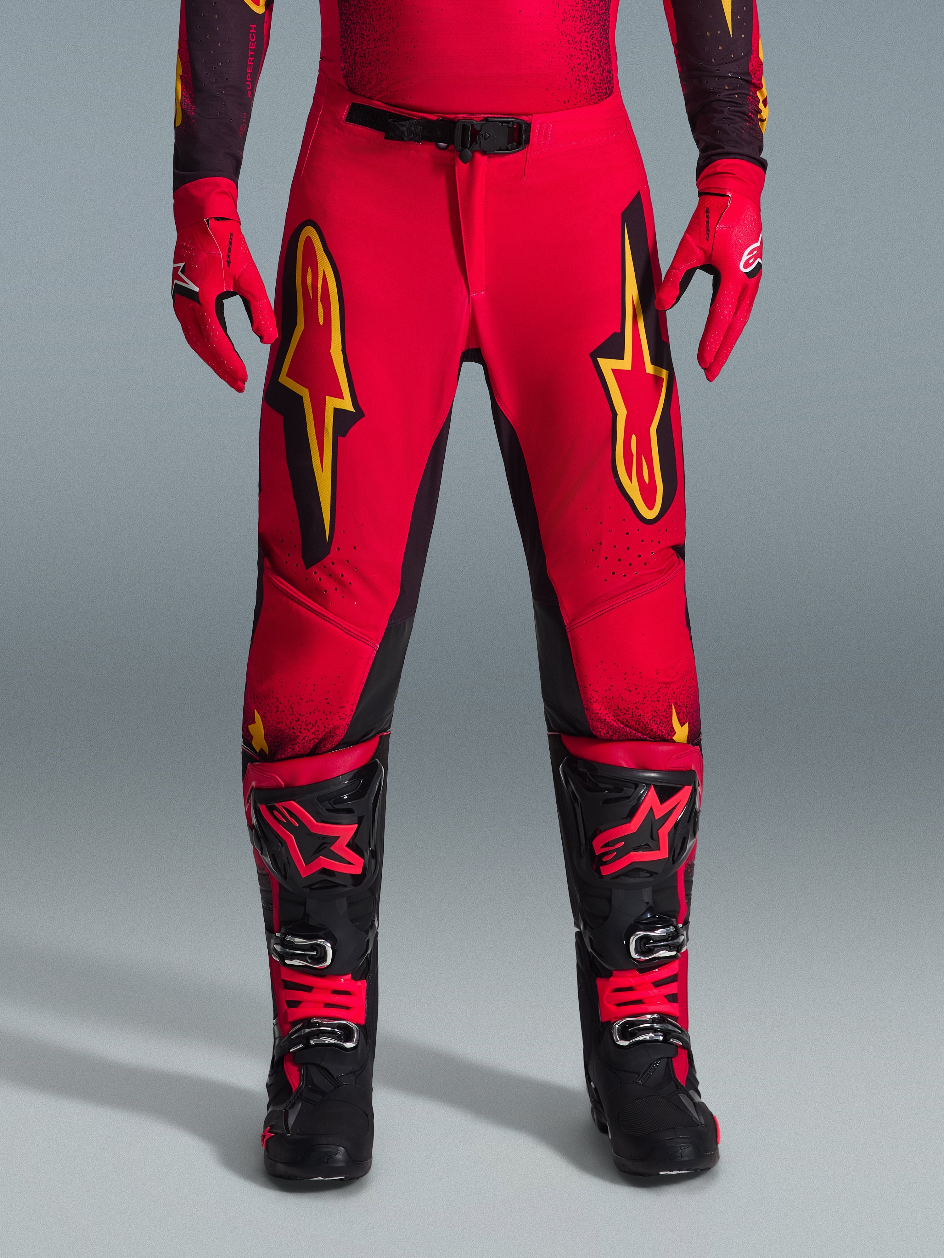 Alpinestars 2026 Supertech Scenz Pants, pantaloni da motocross, rosso, nero e giallo, vestibilità atletica professionale con grandi loghi a stella gialli sulle cosce, abbinati a guanti rossi coordinati e stivali tecnici neri e rossi, progettati per prestazioni d'eccellenza nel fuoristrada