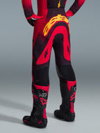 Alpinestars 2026 Supertech Scenz Pants, pantaloni da motocross, rosso, nero e giallo, vista posteriore che mostra il grande logo Alpinestars giallo sulla seduta, indossati con maglia coordinata e stivali da motocross rossi e neri.
