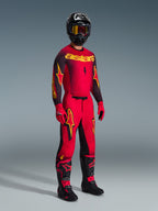 Pantaloni Alpinestars Supertech Scenz 2026, pantaloni da motocross, rosso, nero e giallo, indossati da un pilota in un set completo da gara con maglia e stivali coordinati, con audaci loghi a stella gialli e neri e vestibilità atletica