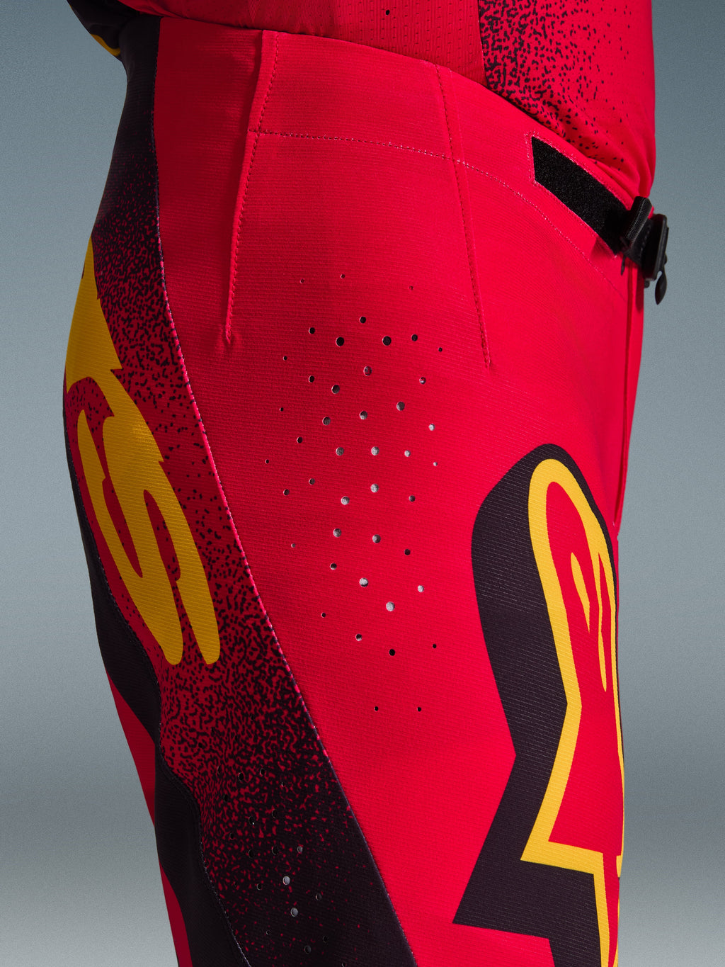 Alpinestars Supertech Scenz 2026, pantaloni da motocross, rosso, nero e giallo, vista laterale ravvicinata con perforazioni di ventilazione laser, loghi grafici e tessuto rip-stop elastico per gare di motocross