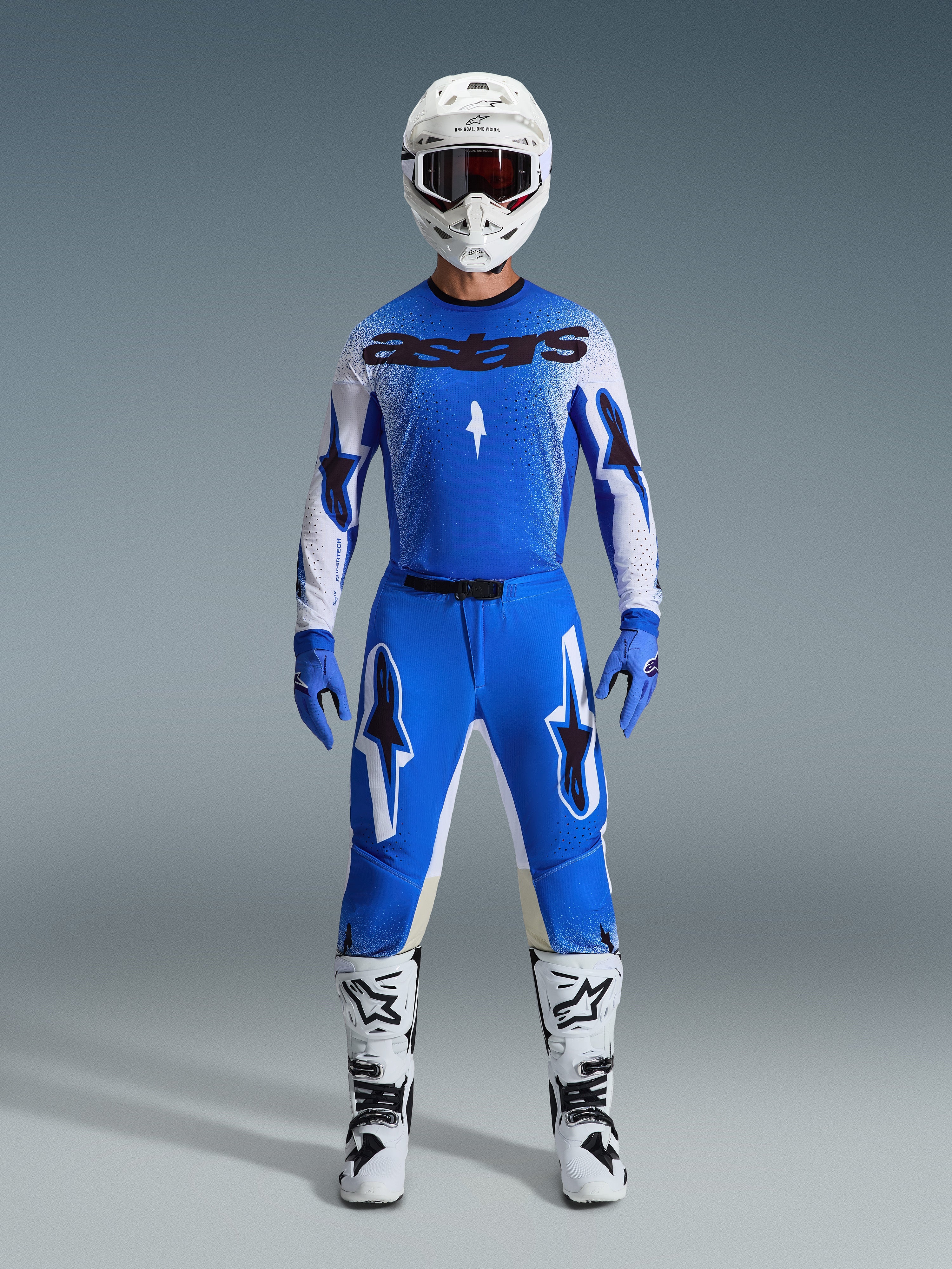 Set completo Alpinestars Supertech Scenz 2026, abbigliamento da motocross, blu Ucla e bianco, outfit da gara con maglia blu e logo 'astars' nero, pantaloni coordinati con grafiche a stella, casco bianco con occhiali scuri, guanti blu e stivali bianchi con dettagli neri