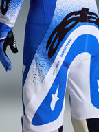 Alpinestars 2026 Supertech Scenz Pants, pantaloni da motocross, blu UCLA e bianco, primo piano del lato e del retro che mostra il grande logo A-star nero e il marchio 'SUPERTECH', con zone di ventilazione traforate e tessuto elasticizzato resistente