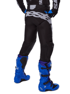 Alpinestars Pantaloni Racer Graphite 2025, pantaloni da motocross, nero e grigio, vista posteriore con grande logo grigio sulla seduta, indossati con stivali da motocross blu acceso e maglia nera e blu, abbigliamento da gara fuoristrada resistente