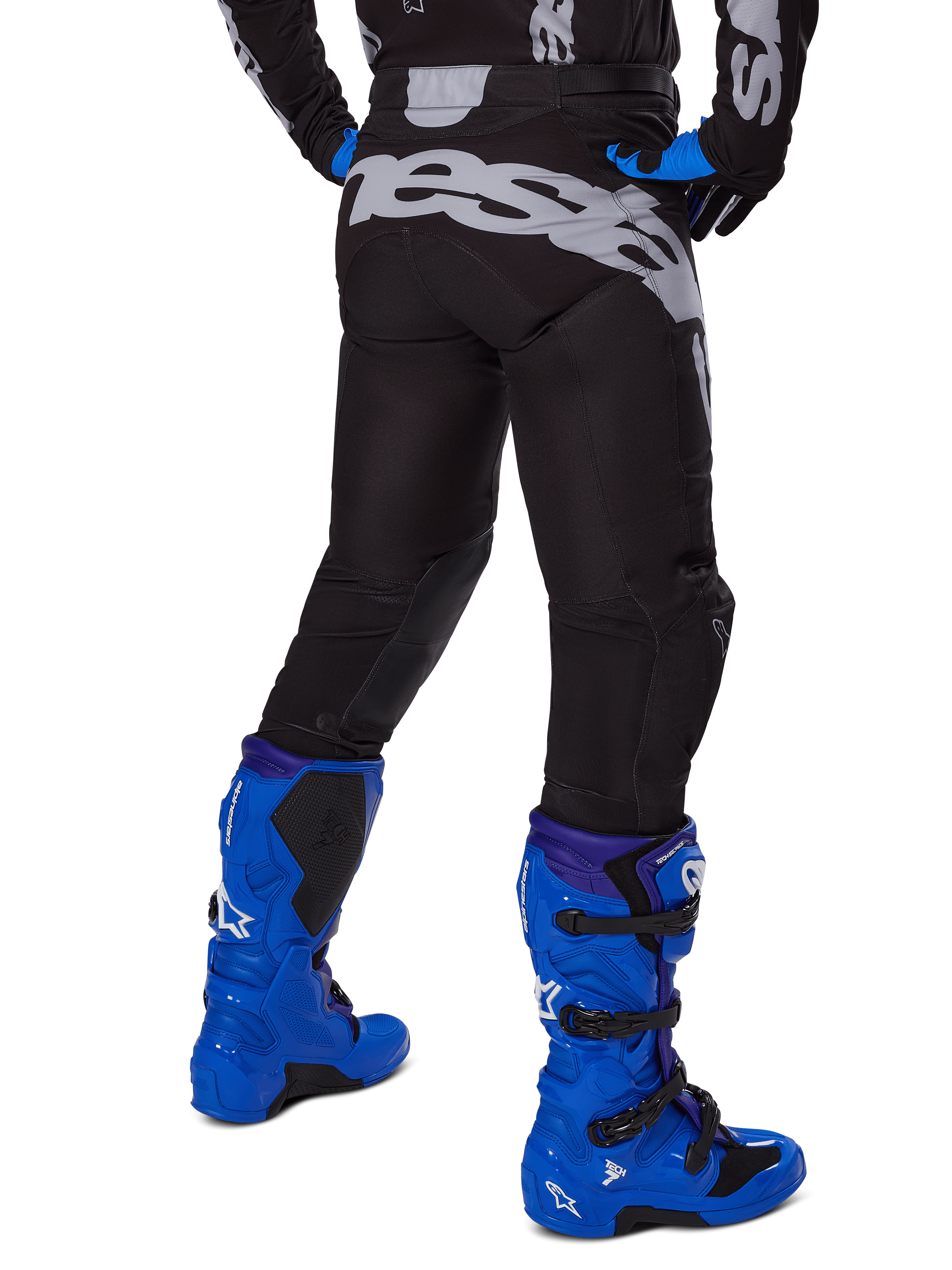 Alpinestars Pantaloni Racer Graphite 2025, pantaloni da motocross, nero e grigio, vista posteriore con grande logo grigio sulla seduta, indossati con stivali da motocross blu acceso e maglia nera e blu, abbigliamento da gara fuoristrada resistente