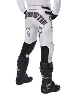 Alpinestars Racer Hollow 2025, pantaloni da motocross, Light Camo Brown, vista posteriore del pilota con grande marchio sulla seduta e pannelli elasticizzati neri sulla parte inferiore delle gambe, abbinati a stivali Tech 7 neri
