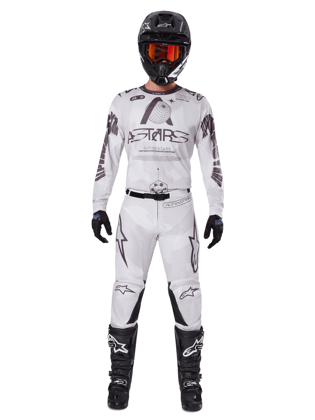 Pilota di motocross con pantaloni Alpinestars 2025 Racer Hollow in Light Camo Brown, maglia a maniche lunghe coordinata bianca e grigia, casco nero con occhiali arancione-rossi, guanti e stivali neri, completo da gara per prestazioni off-road